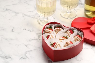 Photo of Delicious chocolate covered strawberries in heart shaped box and sparkling wine on white marble table. Space for text