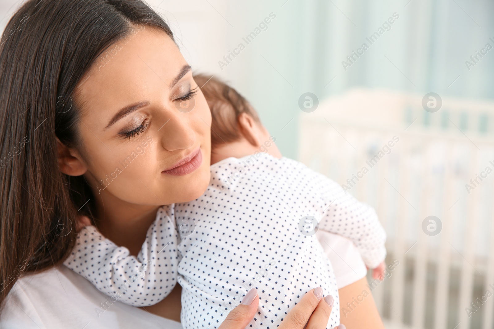 Photo of Woman holding her baby in light nursery. Space for text