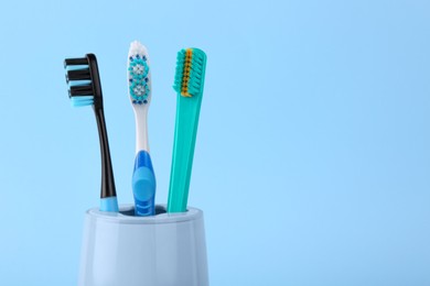Photo of Different toothbrushes in holder on light blue background, closeup. Space for text