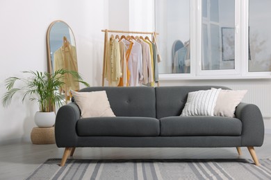 Photo of Stylish living room interior with comfortable grey sofa and clothing rack