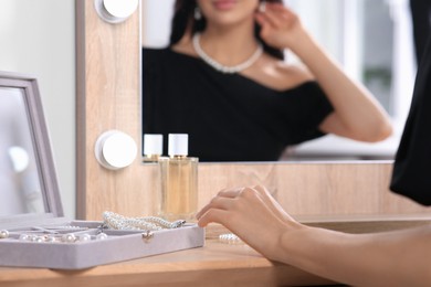 Photo of Young woman with elegant pearl jewelry at dressing table indoors, closeup