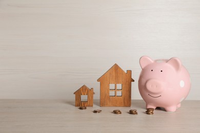 Photo of Piggy bank, stacked coins and house models on white wooden table. Space for text