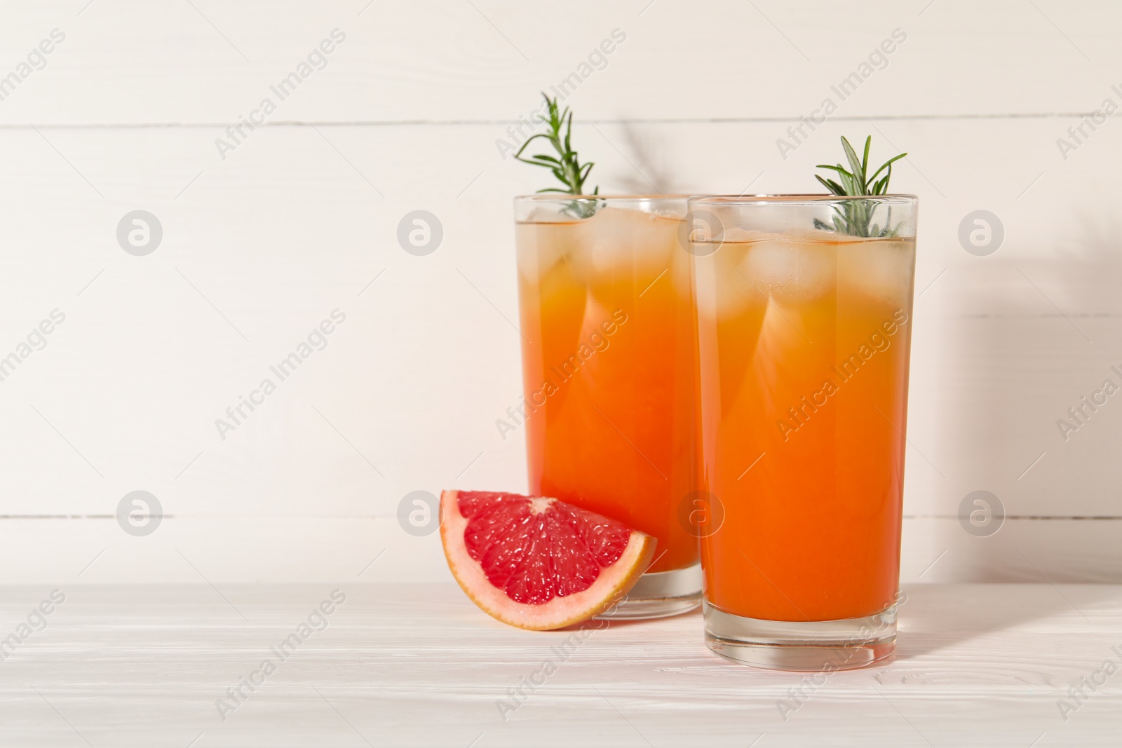 Photo of Tasty grapefruit drink with ice and rosemary in glasses on white wooden table. Space for text