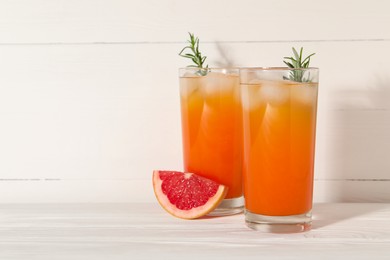 Photo of Tasty grapefruit drink with ice and rosemary in glasses on white wooden table. Space for text