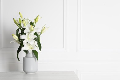 Photo of Beautiful bouquet of lily flowers in vase on light table near white wall, space for text