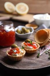 Delicious tartlets with red caviar and cream cheese served on wooden board, closeup