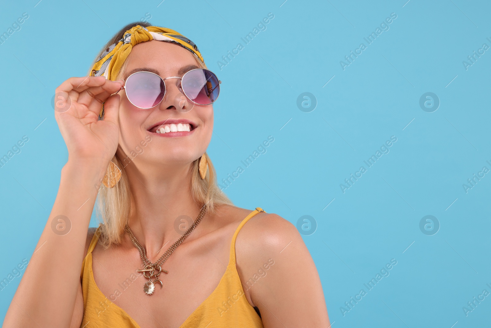 Photo of Portrait of smiling hippie woman in sunglasses on light blue background. Space for text