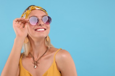 Portrait of smiling hippie woman in sunglasses on light blue background. Space for text