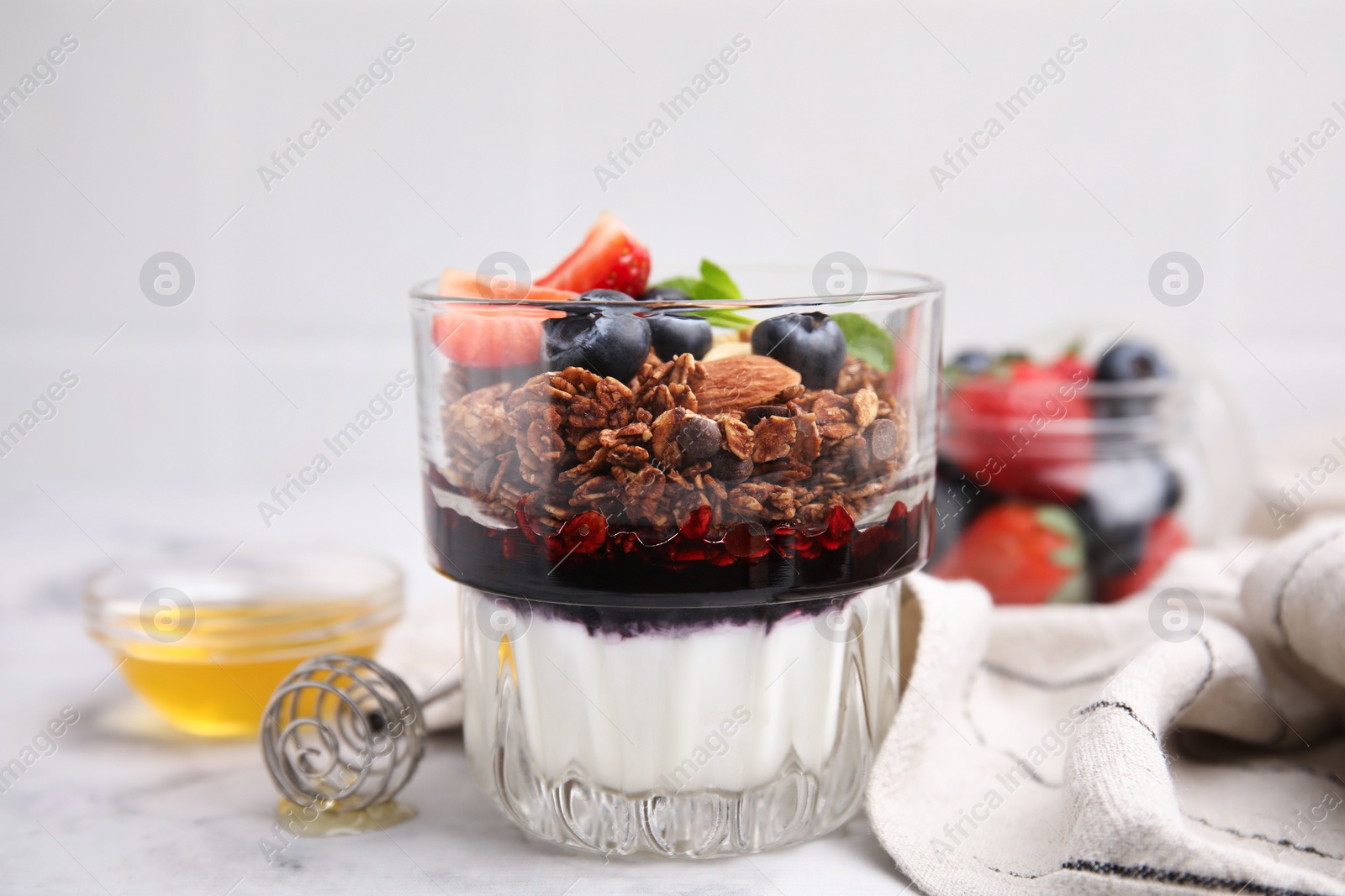 Photo of Tasty granola with berries, jam and yogurt in glass on white table