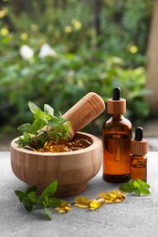 Photo of Wooden mortar with fresh green herbs, extracts and capsules on light grey table outdoors, space for text