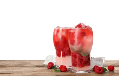 Glasses of raspberry refreshing drink with ice cubes on wooden table against white background