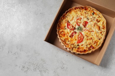 Photo of Tasty quiche with tomatoes and cheese in open box on light table, top view. Space for text