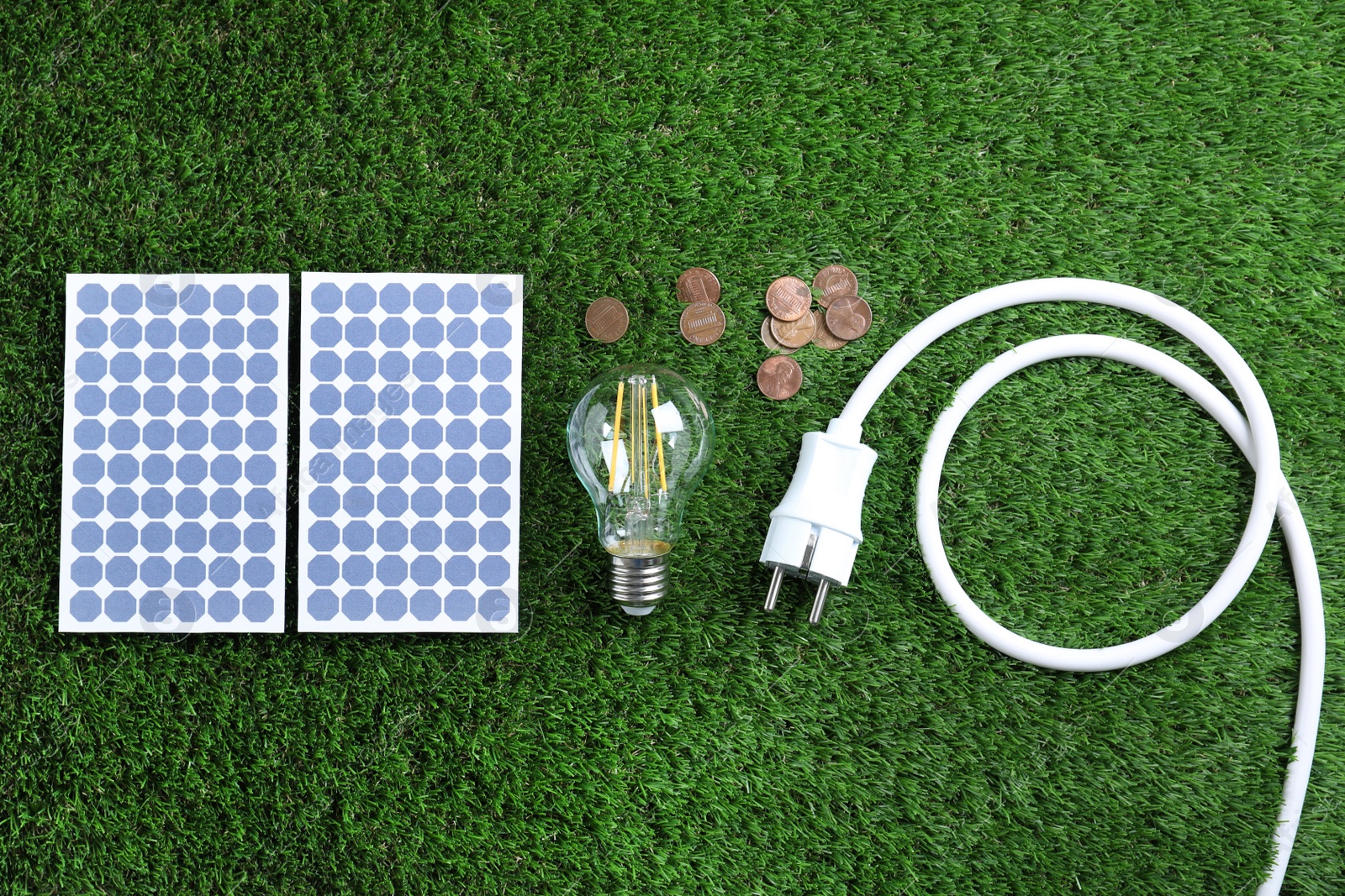 Photo of Flat lay composition with solar panels, light bulb and coins on green grass