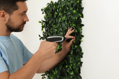 Photo of Man with screwdriver installing green artificial plant panel on white wall