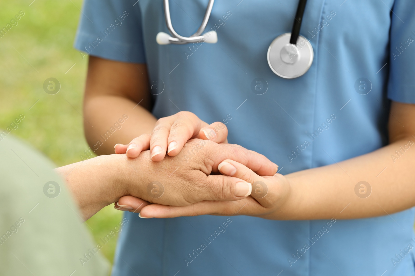 Photo of Elderly woman and female caregiver holding hands outdoors, closeup