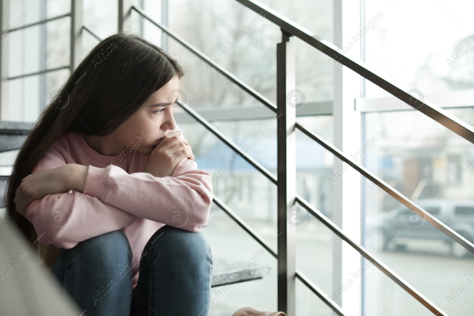 Photo of Upset teenage girl sitting on stairs indoors. Space for text