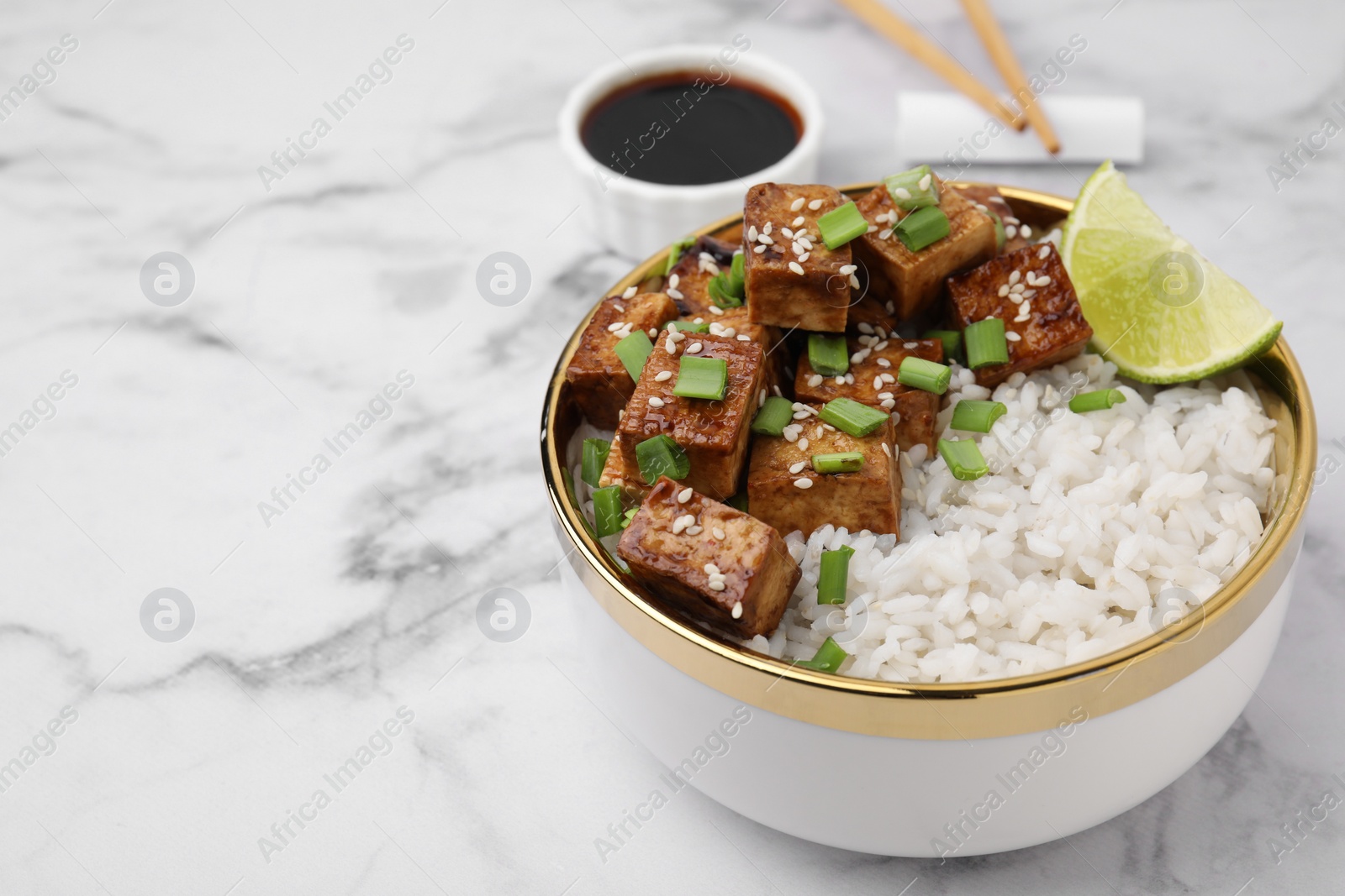 Photo of Bowl of rice with fried tofu and green onions on white marble table, closeup. Space for text