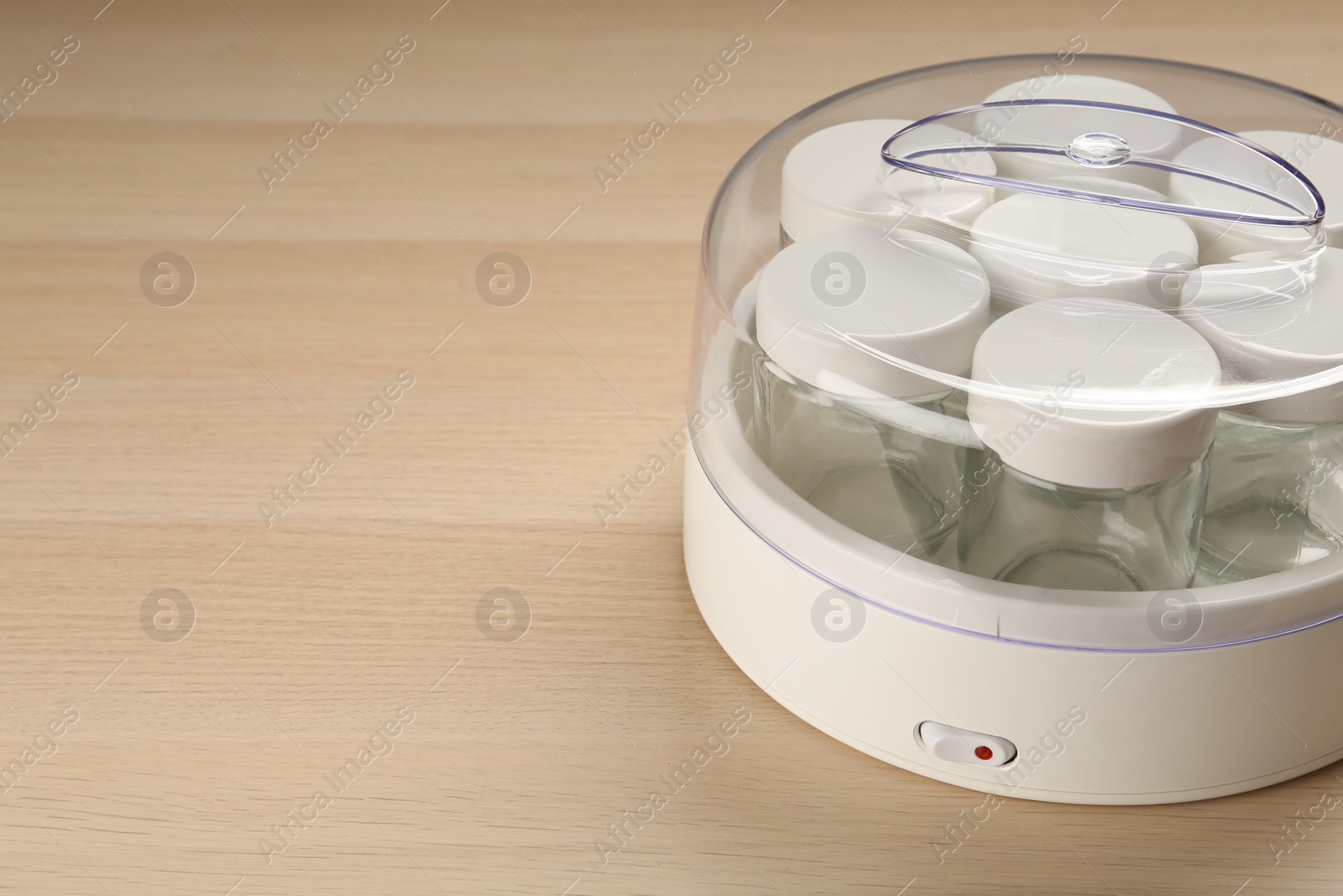 Photo of Modern yogurt maker with empty jars on wooden table. Space for text