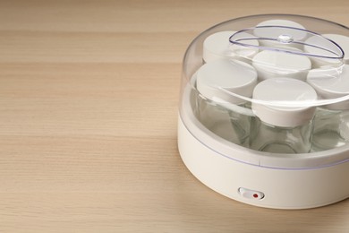 Modern yogurt maker with empty jars on wooden table. Space for text