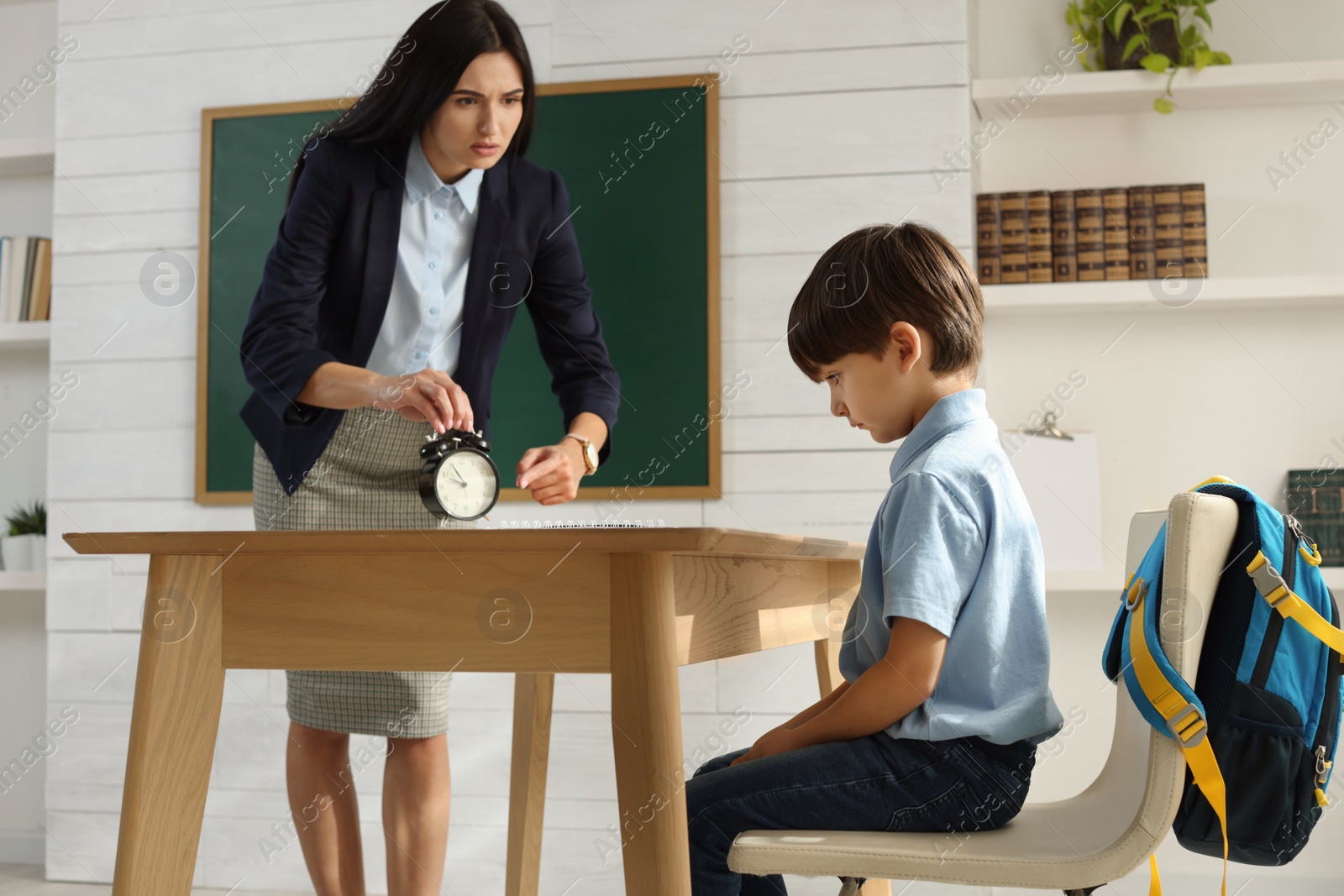 Photo of Teacher with alarm clock scolding pupil for being late in classroom