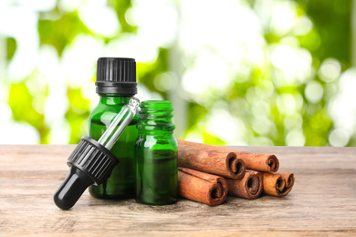 Image of Bottles of essential oil and cinnamon sticks on wooden table against blurred background