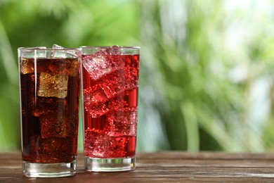 Glasses of different refreshing soda water with ice cubes on wooden table outdoors, space for text