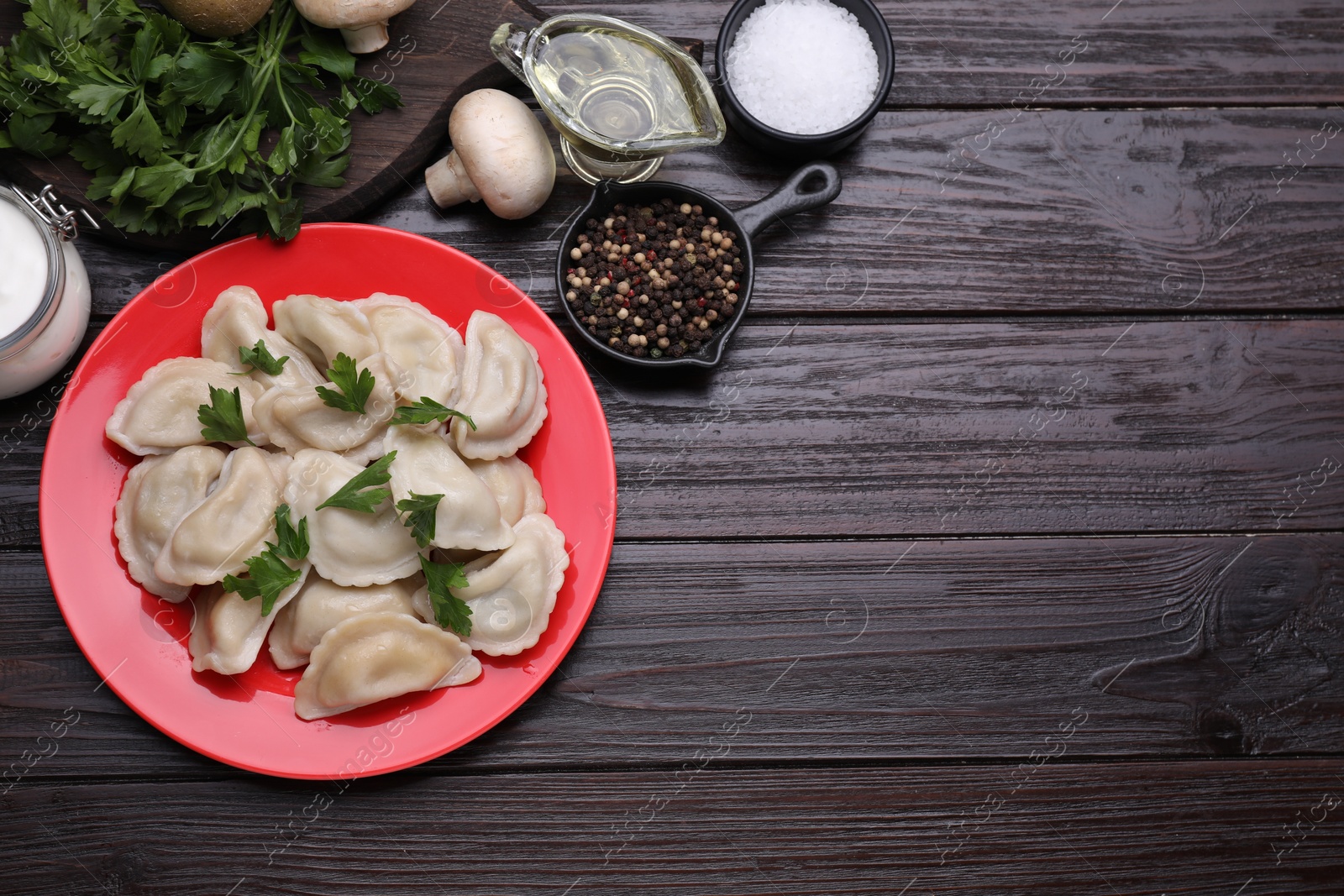 Photo of Delicious dumplings (varenyky) with potatoes and parsley served on brown wooden table, flat lay. Space for text