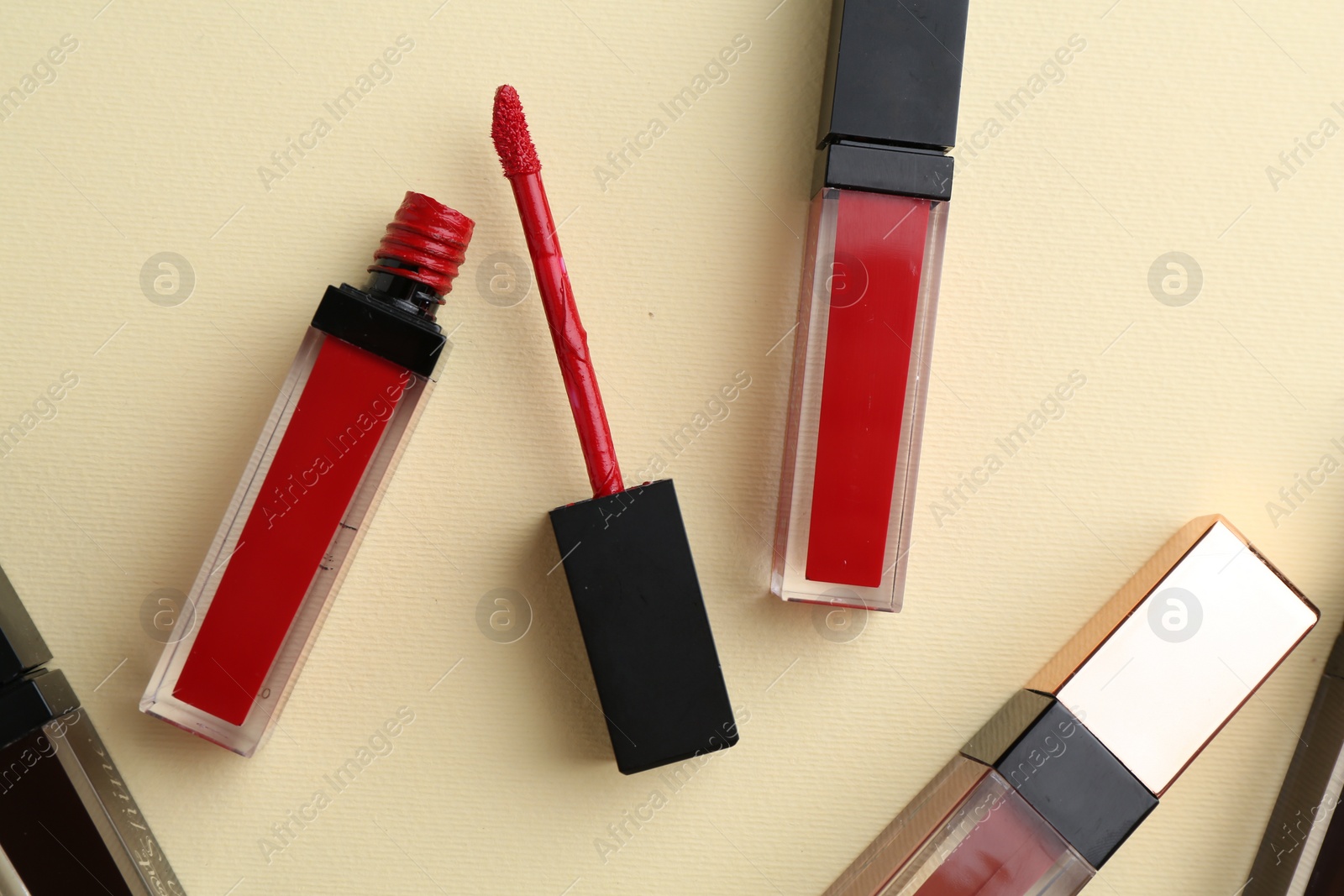 Photo of Different lip glosses and applicator on pale yellow background, flat lay