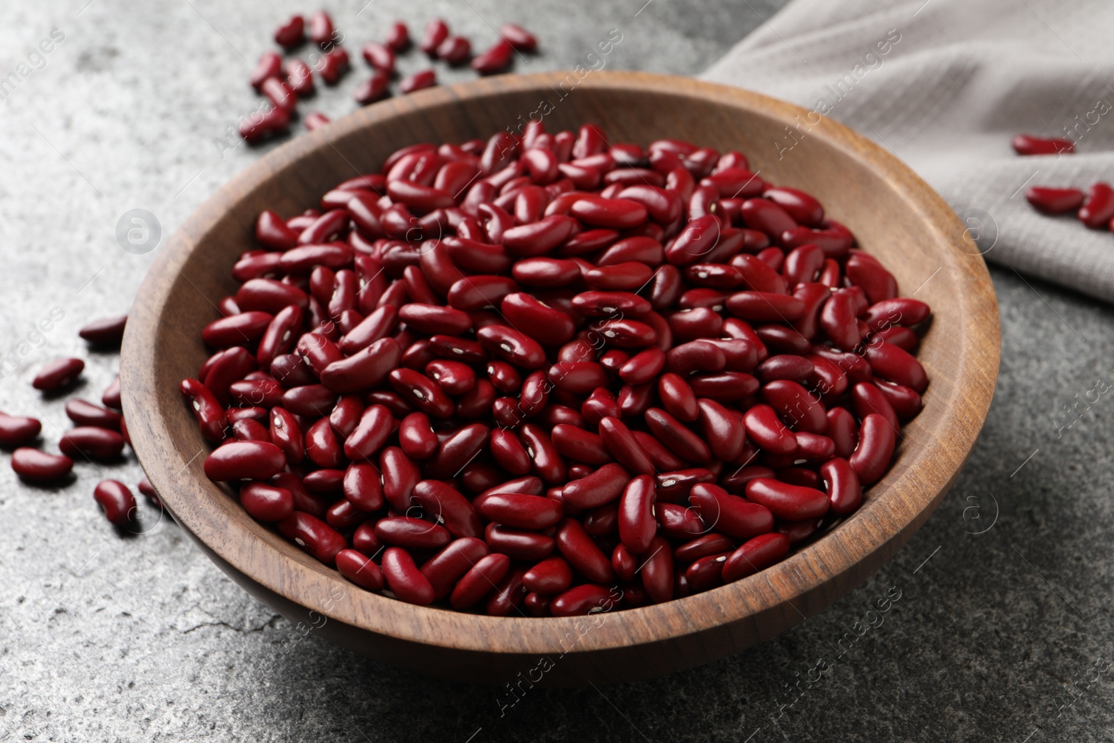 Photo of Raw red kidney beans in wooden bowl on grey table, closeup
