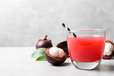 Photo of Delicious fresh mangosteen juice in glass on light grey table, space for text