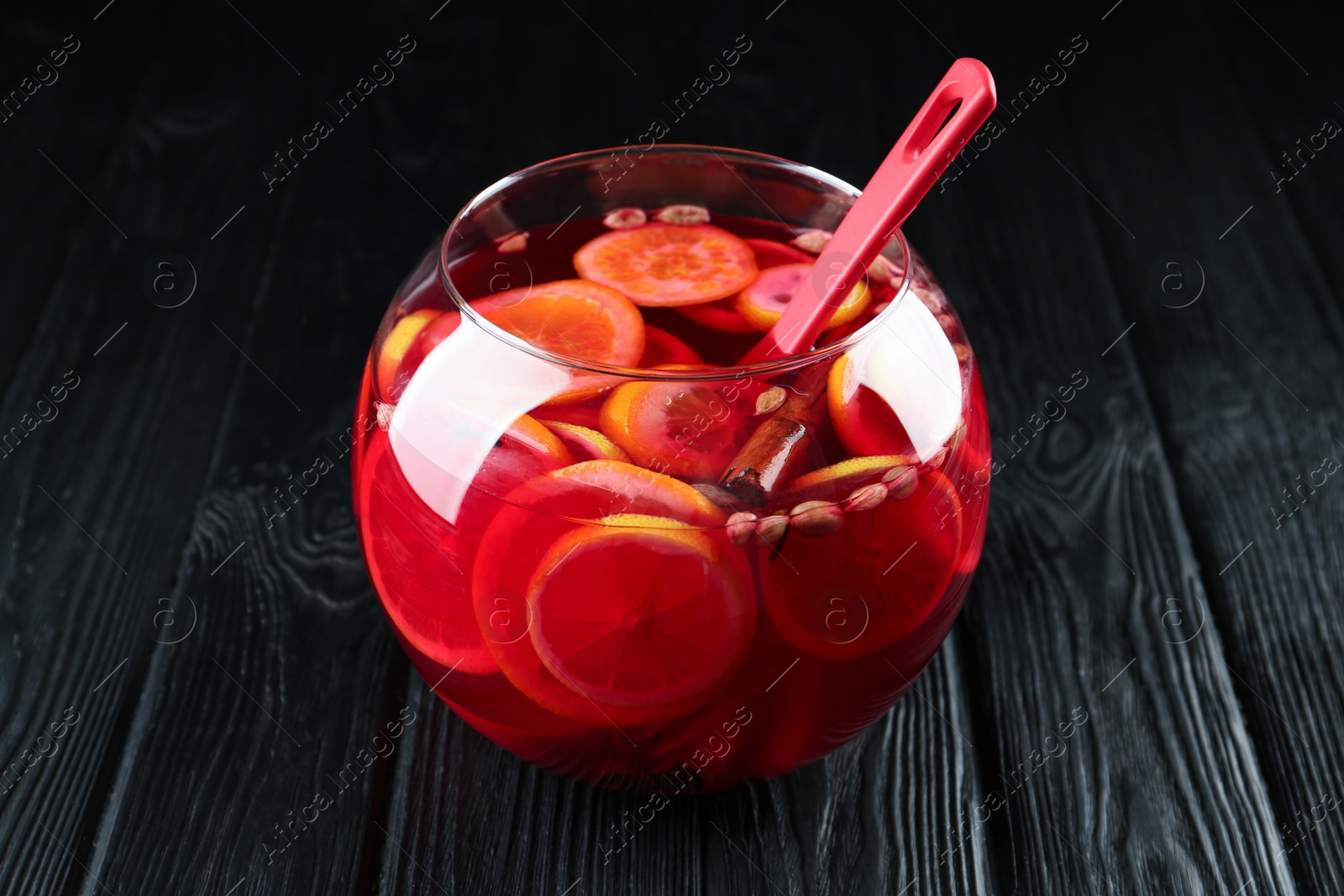 Photo of Glass bowl and ladle of delicious aromatic punch drink on black wooden table