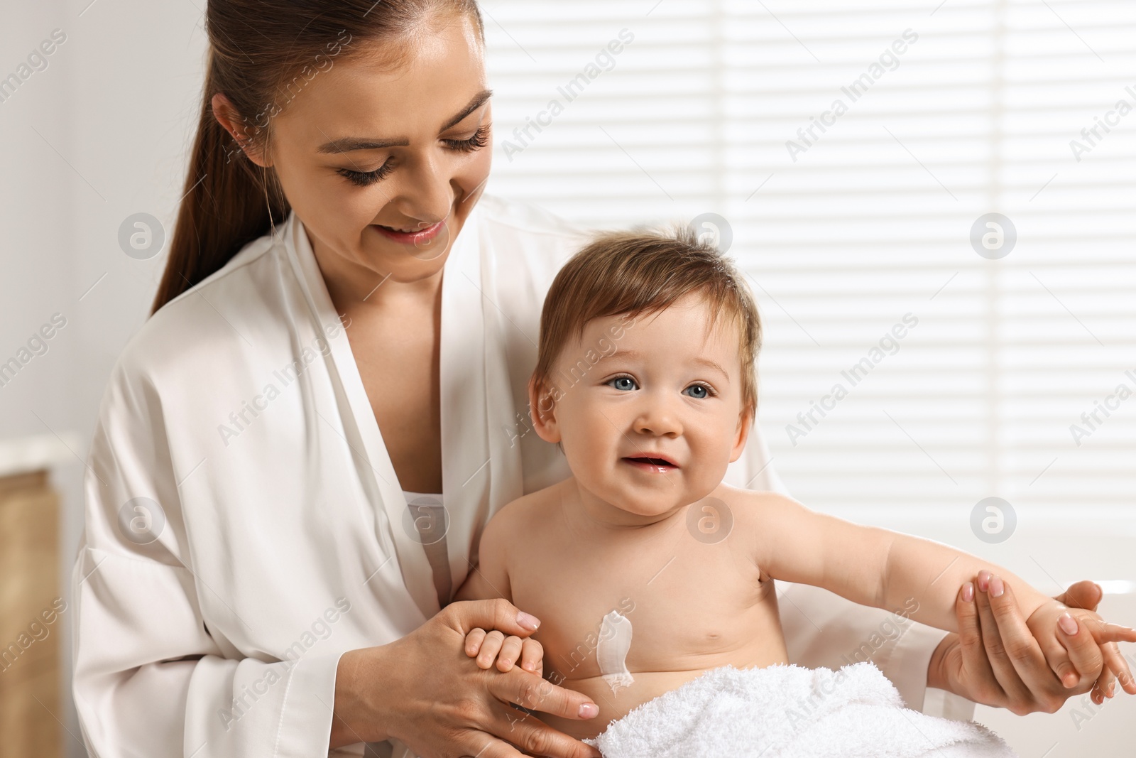 Photo of Happy mother holding her baby with body cream on skin at home