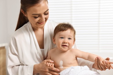 Happy mother holding her baby with body cream on skin at home