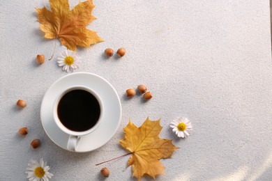 Flat lay composition with cup of hot drink and autumn leaves on light grey textured table. Space for text