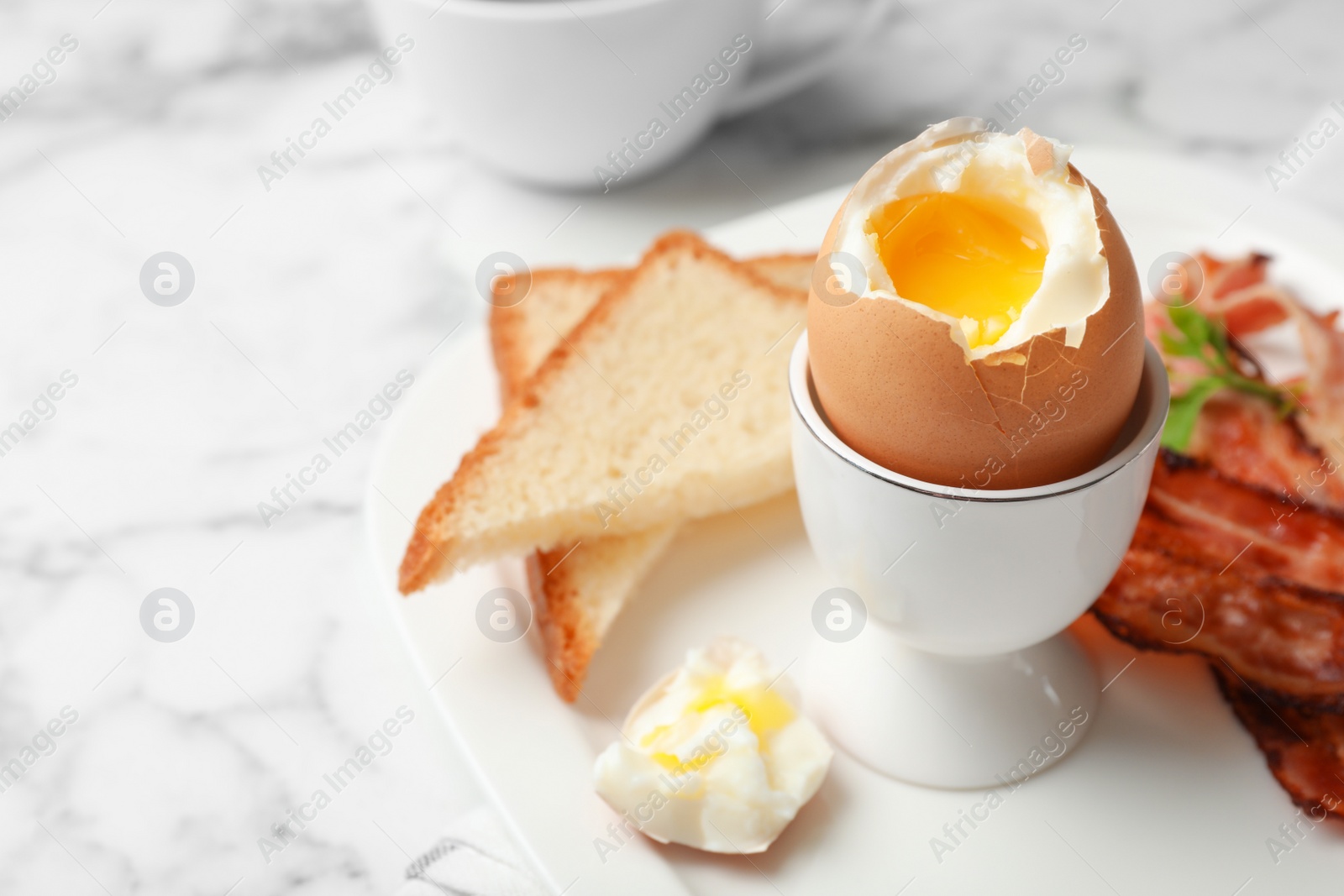 Photo of Holder with soft boiled egg, bread and bacon on plate. Space for text