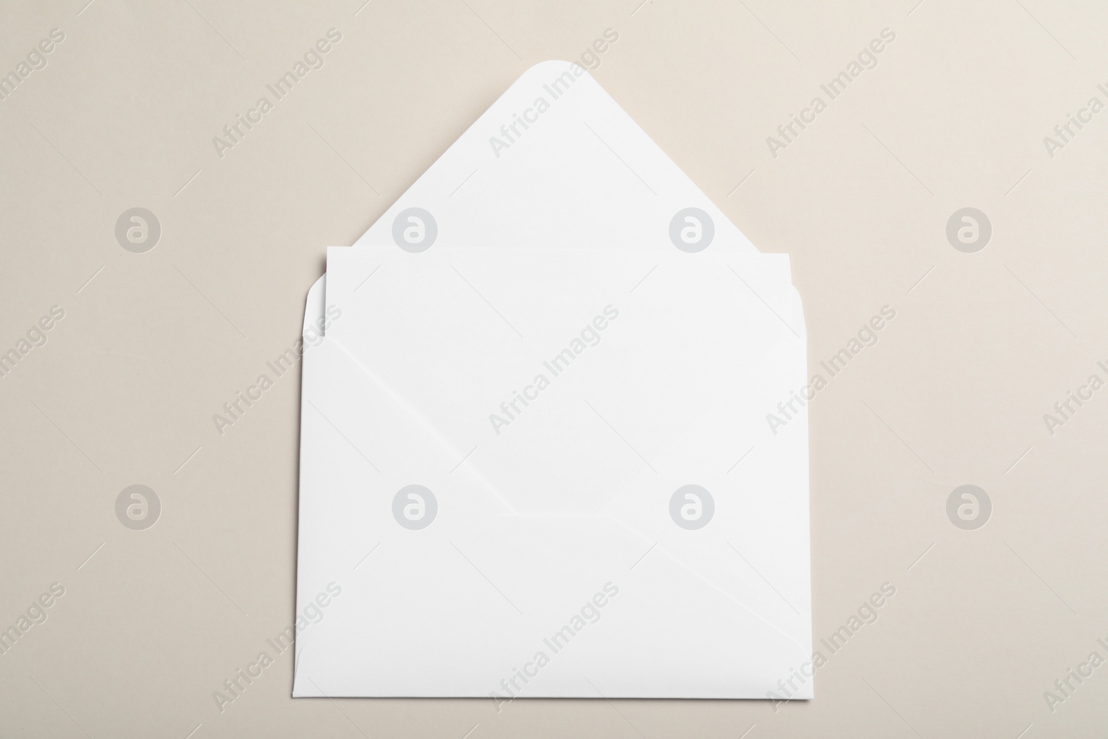 Photo of White paper envelope with blank card on beige background, top view