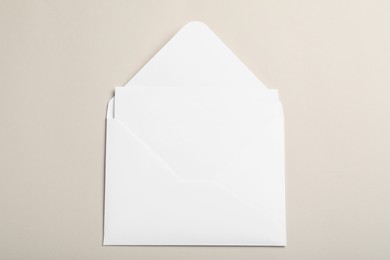 Photo of White paper envelope with blank card on beige background, top view