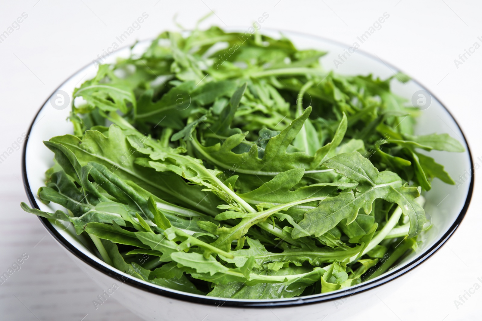 Photo of Fresh arugula in bowl on white table, closeup