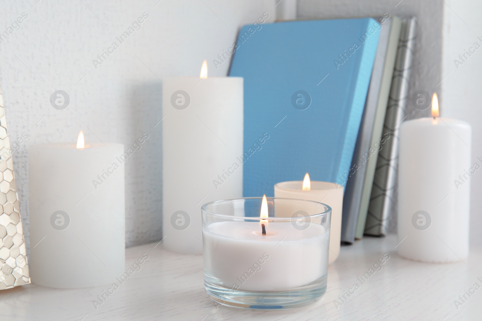 Photo of Burning aromatic candles in holders on bookshelf