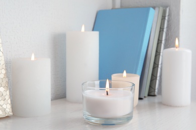 Photo of Burning aromatic candles in holders on bookshelf