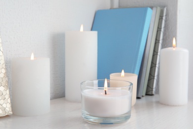 Burning aromatic candles in holders on bookshelf