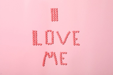Photo of Phrase I Love Me made of heart shaped sprinkles on pink background, flat lay
