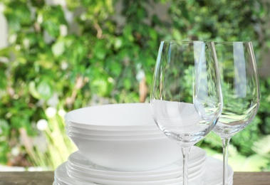 Photo of Clean dishes and glasses on wooden table against blurred background