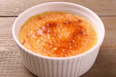 Photo of Delicious creme brulee in bowl on wooden table, closeup