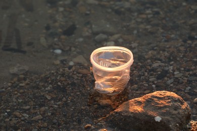 Photo of Used plastic cup in water outdoors, space for text. Environmental pollution concept