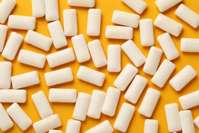 Photo of Many chewing gum pieces on orange background, flat lay