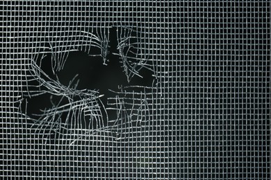 Torn window screen against black background, closeup