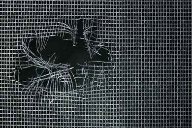 Photo of Torn window screen against black background, closeup