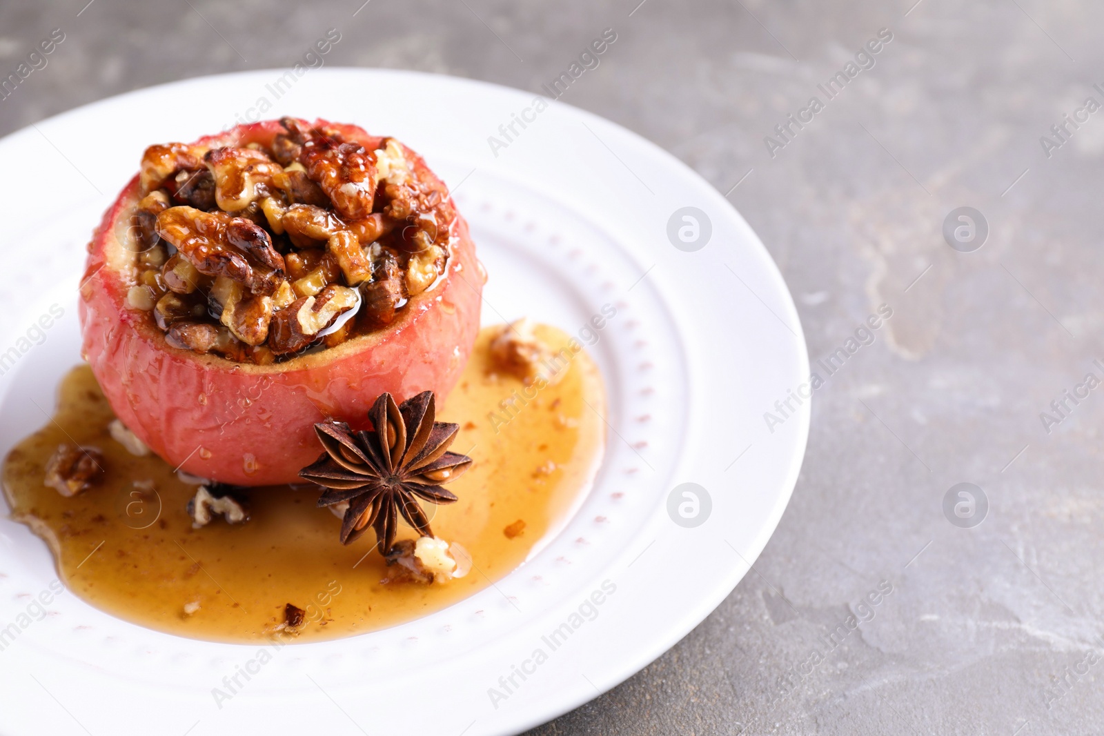 Photo of Tasty baked apple with nuts, honey and anise on gray table, closeup