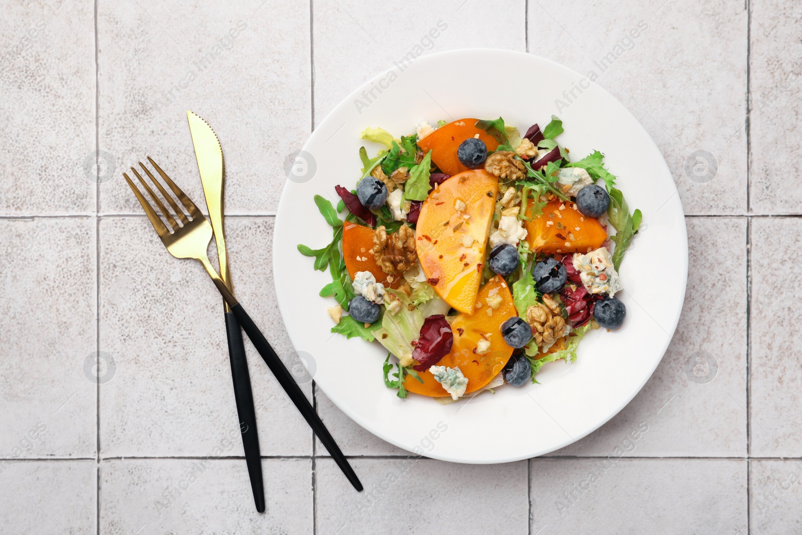 Photo of Delicious persimmon salad, fork and knife on tiled surface, flat lay